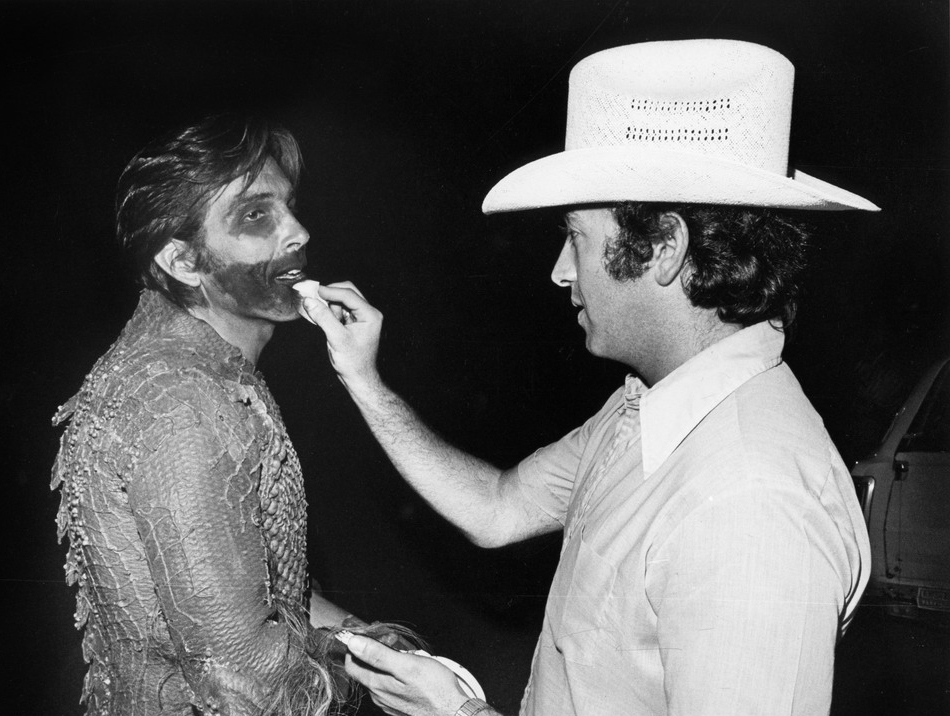Stan Winston applies dark camouflage makeup to a background actor on-set