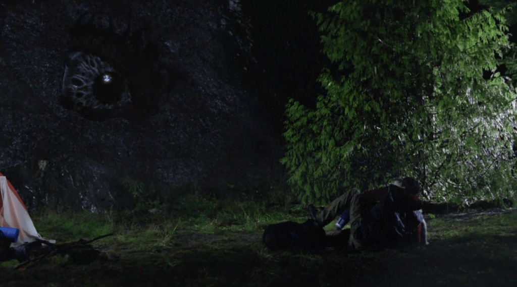 A giant monster eye peers through a hole in the mountainside