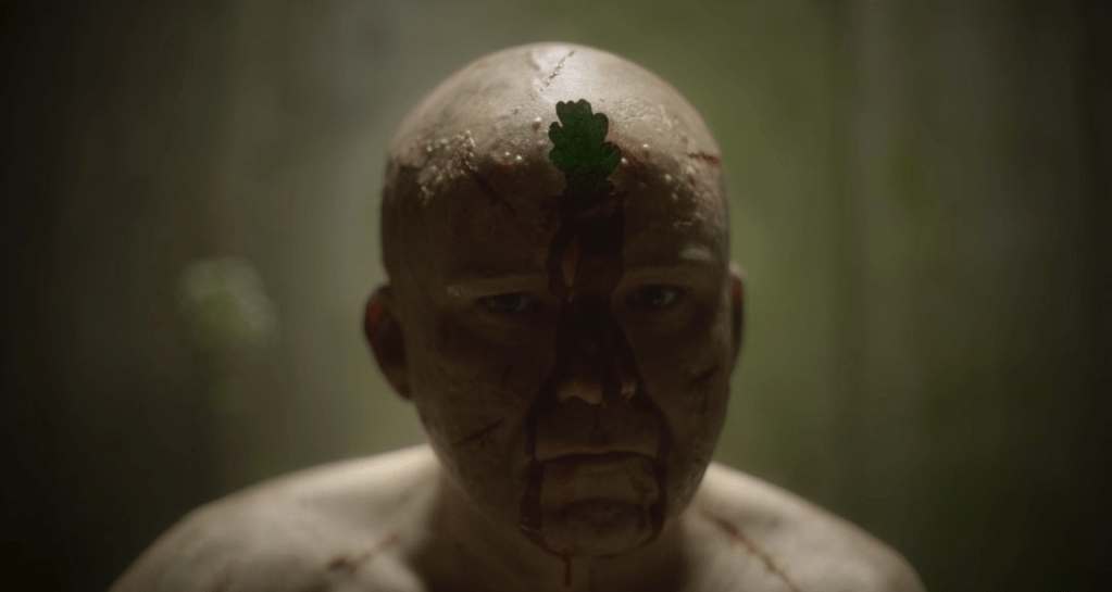 The naked dude starts slitting his skin and inserting leaves...